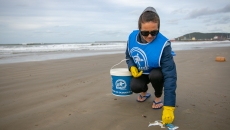 Voluntária recolhe lixo deixado na praia do Porto, em Imbituba